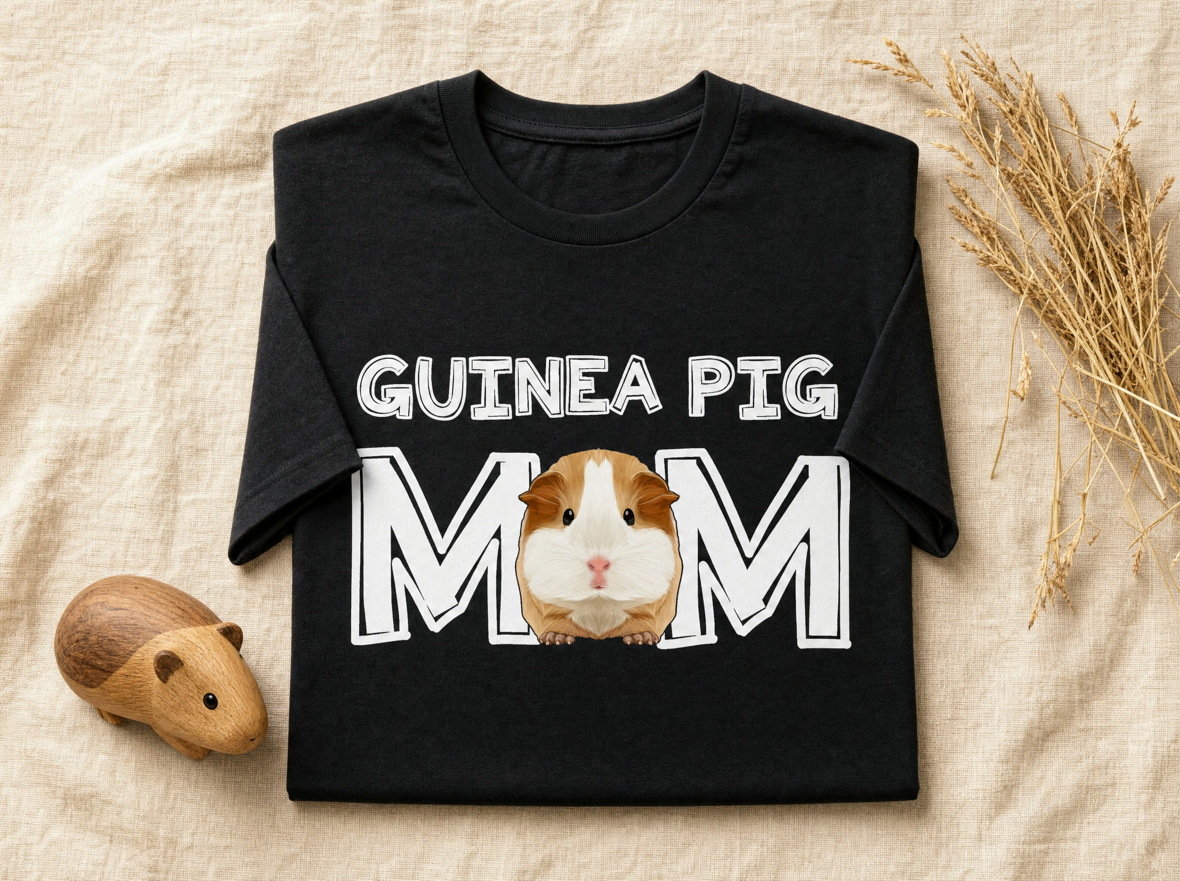 Black Guinea Pig Mom tee folded flat with dried hay and a wooden guinea pig figure