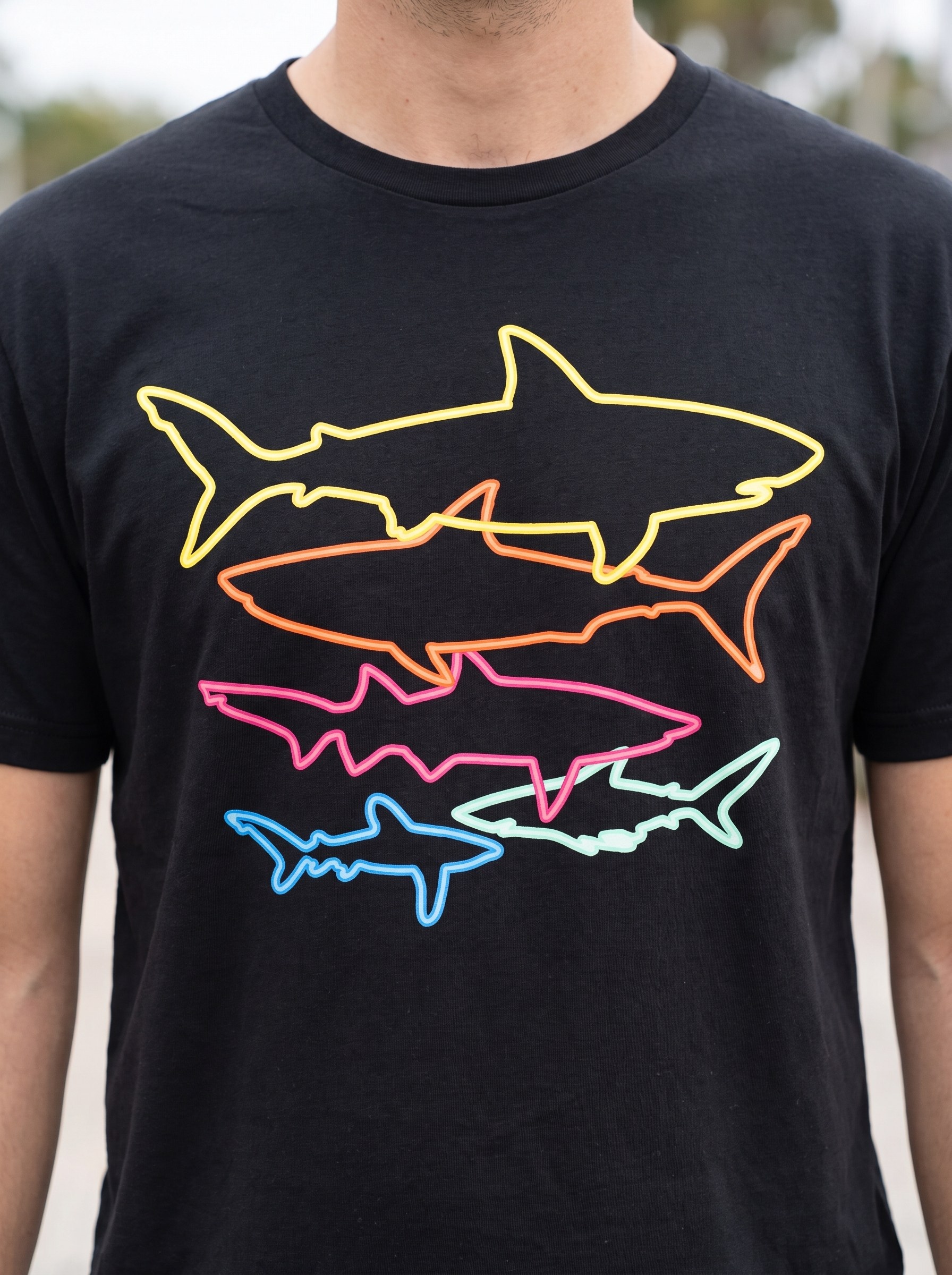 Closeup of the five colorful outline sharks printed flat on the black cotton tee in daylight