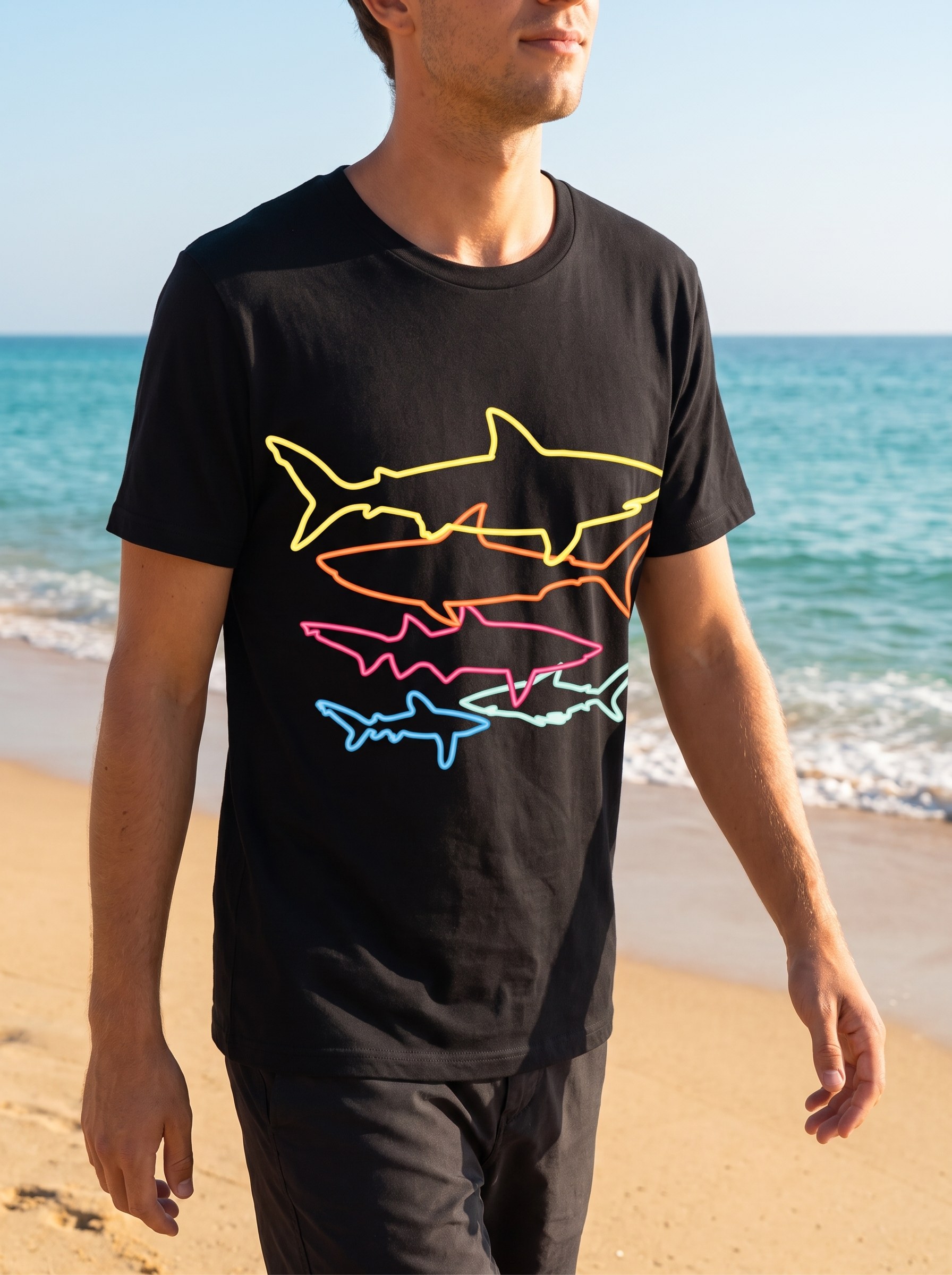 Person wearing the black retro shark tee on a sunny beach walk, the five colorful outline sharks clear on the chest